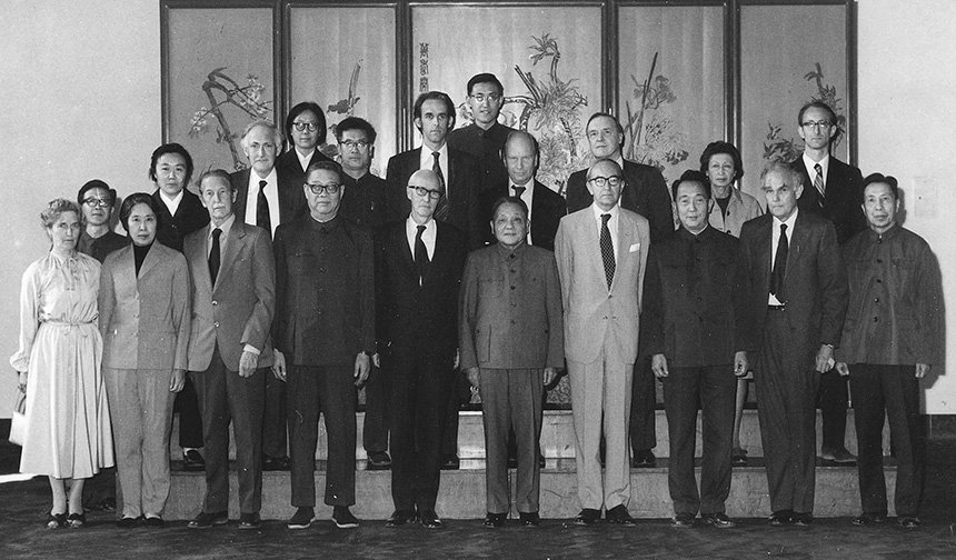A black and white photo of British Academy's delegates in China stood in front of a large traditional Chinese painting