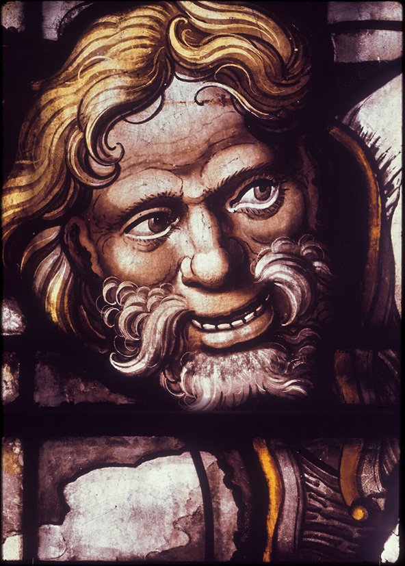 Fragment of a stained glass window from King&#x27;s College Chapel in Cambridge showing the face of a smiling bearded man