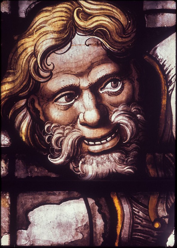 Fragment of a stained glass window from King's College Chapel in Cambridge showing the face of a smiling bearded man