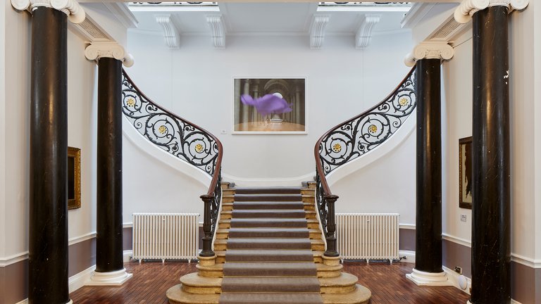 Photo of grand staircase with grey carpet on stone, framed by black columns