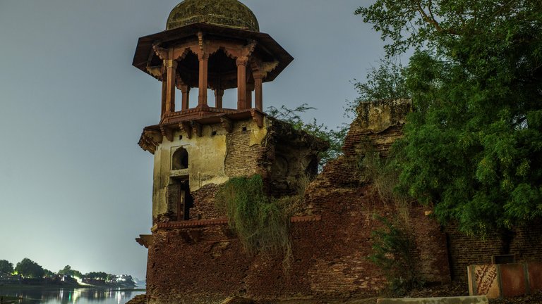 Ruins of an ancient structure with a domed tower near a water body, captured at dusk.