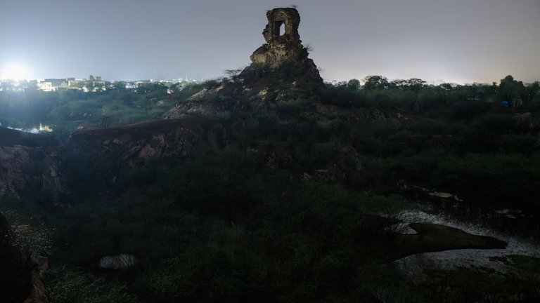 Nighttime view of Feroz Shah Kotla Fort with illuminated surroundings and a distinct rocky formation resembling a large arch at the top.