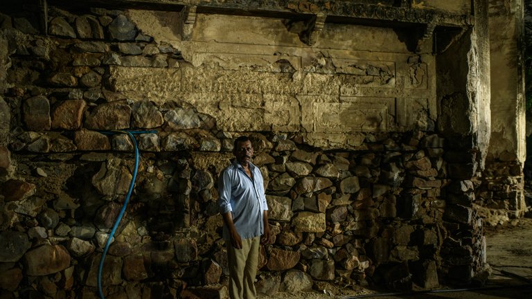 A person stands in front of an ancient stone wall inside the ruins of a village.