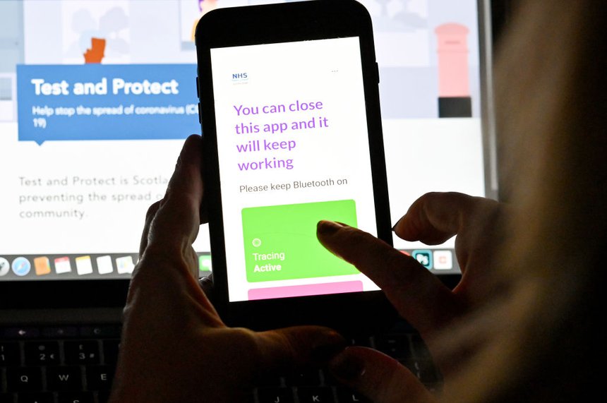 Photograph of a person holding a smartphone screen showing COVID-19 track and trace app.