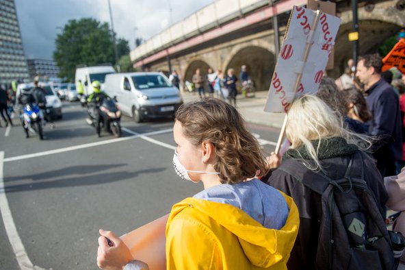 A row of protesters in the bottom right corner of the image, wearing masks and holding protest signs, facing police and onlookers in the top left corner of the image.