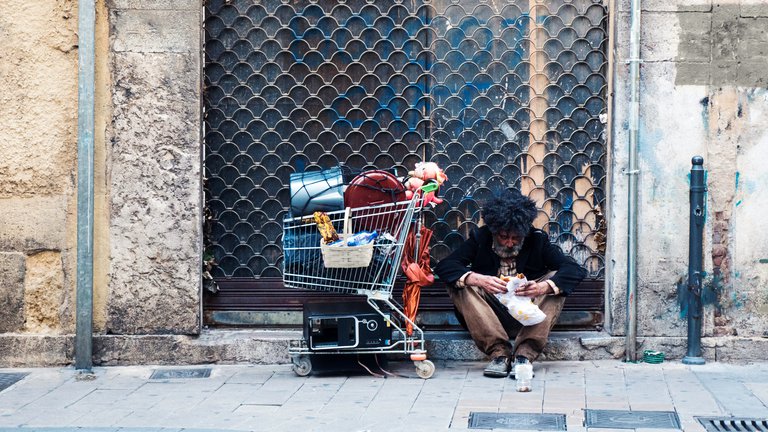 Homeless man with his cart seated at the street eating a sandwich