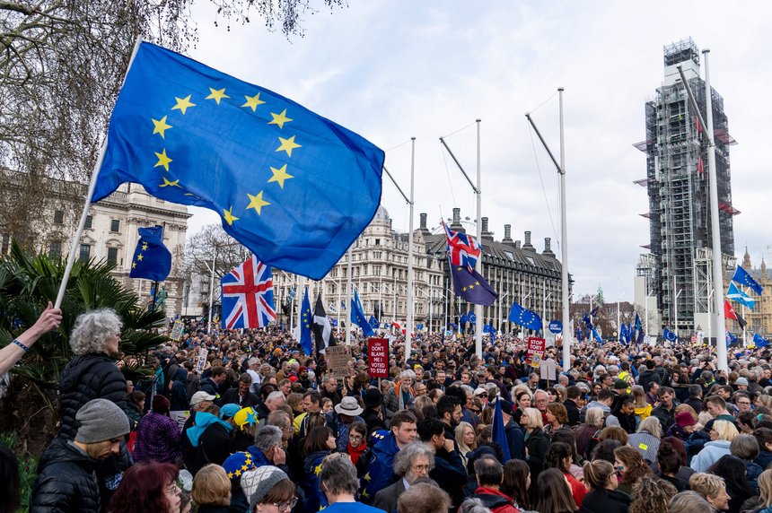 Hundreds of people gathered in Parliament Square at a rally calling for a second referendum on the UK's membership of the European Union. Many EU flags and Union flags are being held up by people in the crowd.