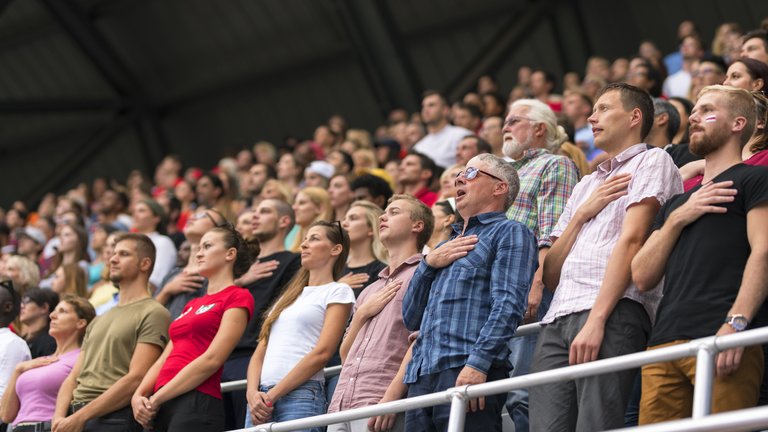 Large crowd in a sports ground speaking in unison with hands on hearts