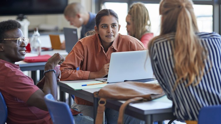 Three university students sitting at a table, engaged in a lively discussion.