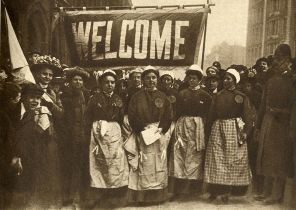 A group of British suffragettes, recently released from prison, with a 'Welcome' banner.