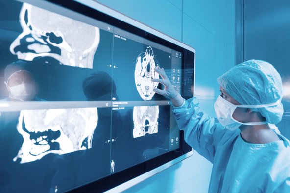 Surgeon in medical PPE looking at brain scans of patient.