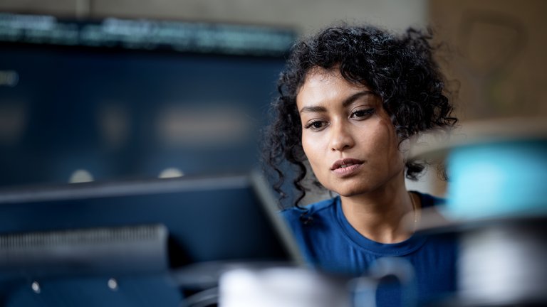 A person sitting at a desk and looking at a laptop screen in focus.