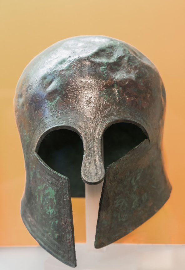 Votive bronze Corinthian style helmet dating from 7th century BC on display at the Delphi Archaeological museum, Phocis, Greece. The helmet is dented and the bronze has a green hue due to oxidisation.