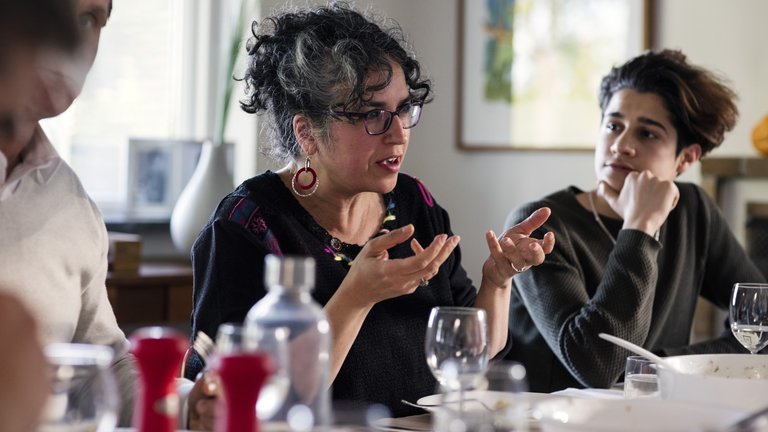 A woman takes part in a discussion among people dining at a table.