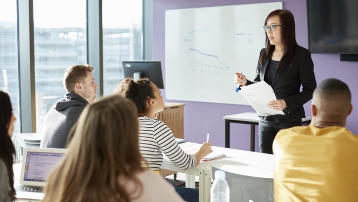 A group of five school pupils in their teens listen to a teacher addressing the class.