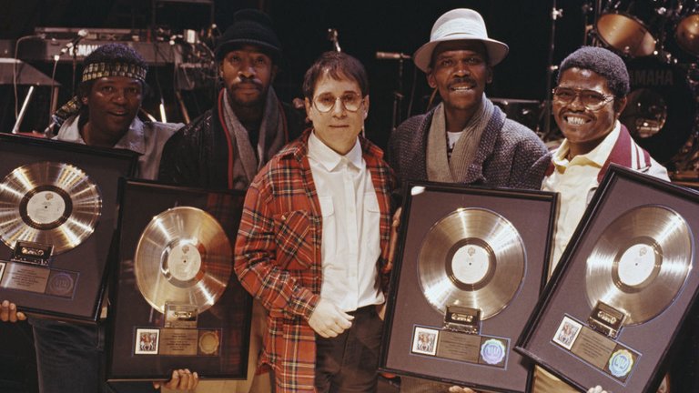 Paul Simon poses with four musicians, all holding gold discs of Paul Simon's album 'Graceland'