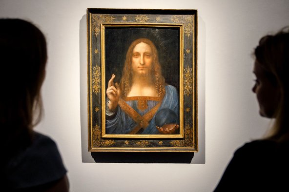 Two people stand in front of the painting 'Salvator Mundi' by Leonardo da Vinci at Christie's before auction.