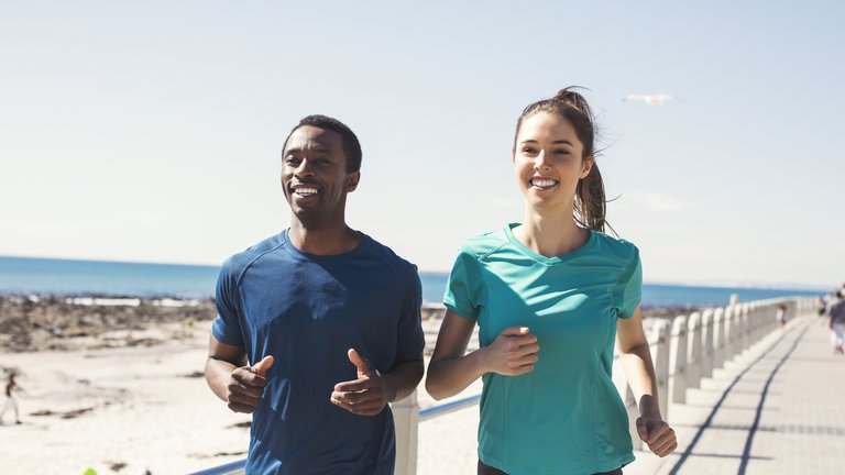 Smiling couple jogging on promenade against sky