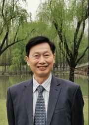 A photo of Zhenzhao Nie FBA outdoors in a suit against a backdrop of trees and a lake