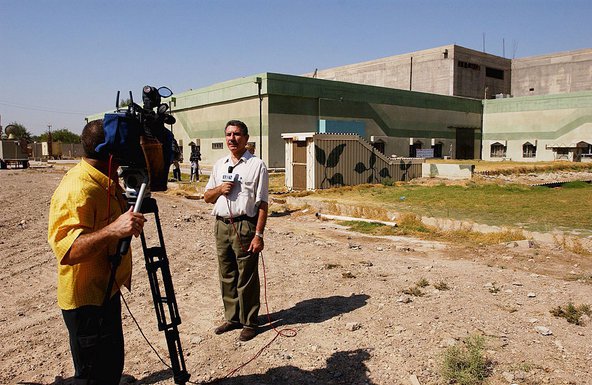 A TV journalist stands in front of the Al Furat military facility in Iraq.