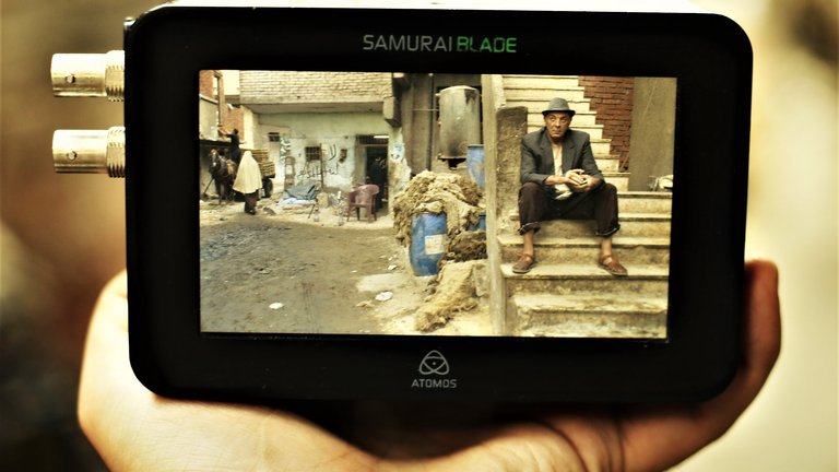 Digital camera screen shows older man sitting on steps next to gravel