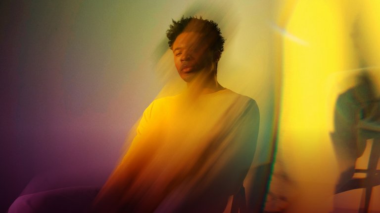 An image of a seated man with a blurred effect and yellow and pink lighting