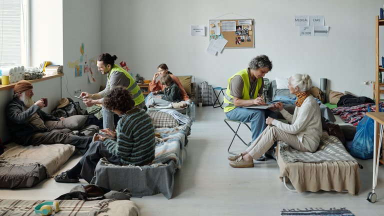 Photo of refugees sitting on beds on the floor at a shelter