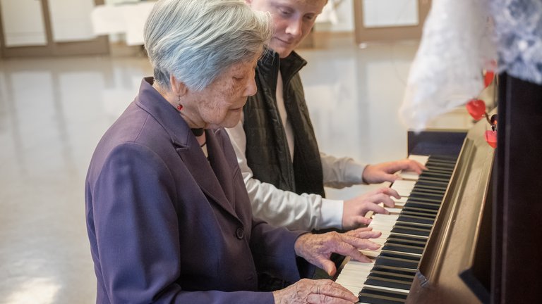 Senior woman playing piano with younger man in music therapy session.