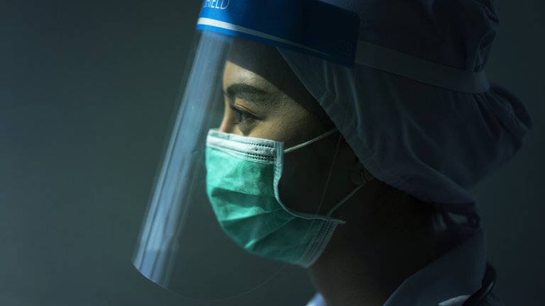 Female doctor in left facing profile wears surgical mask and face shield.