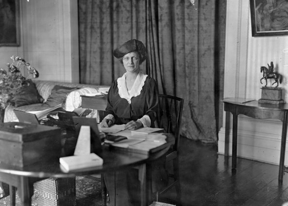 Nancy Astor, sitting at her desk in her office with some books and papers.
