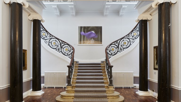 Image of a staircase with a piece of art hanging at the top in the middle.