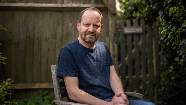 Photograph of Philippe Sands sitting in a chair in a garden