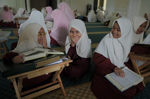 Photograph of three giggling schoolgirls in hijabs sitting in a classroom learning the Quran.