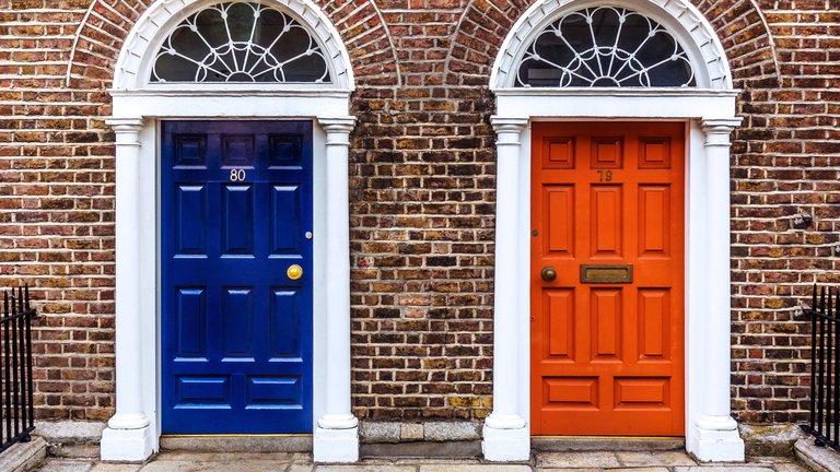 A red door and a blue door side by side, set in brick-built terraced housing.
