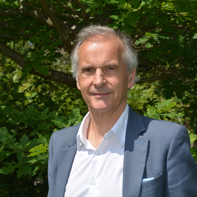 Headshot of Roger Matthews standing in front of trees and greenery