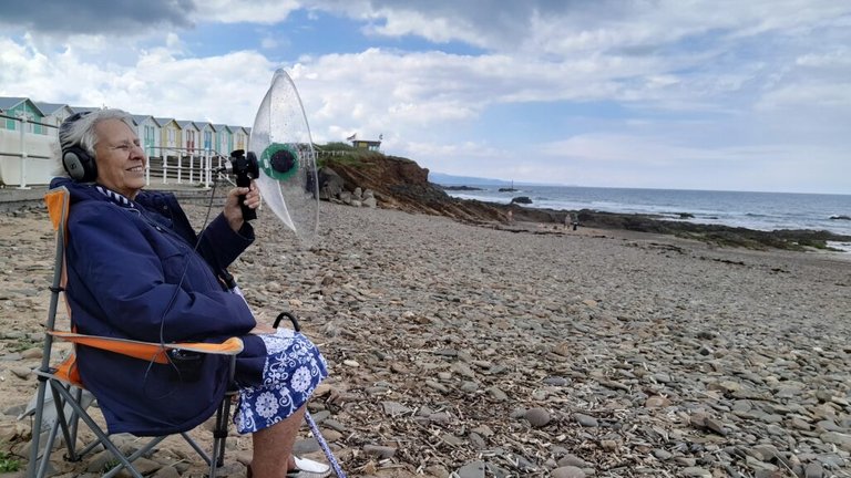 An elderly woman sits on a beach wearing a listening device