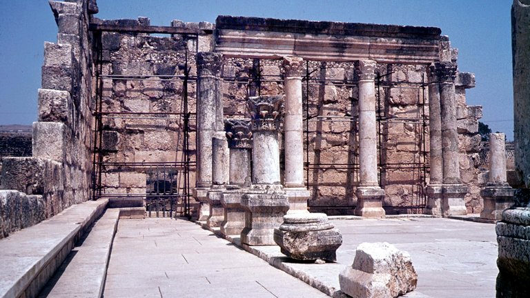 Photograph of ruins of ancient Capernaum synagogue depicting remnants of an ancient building with central pillars