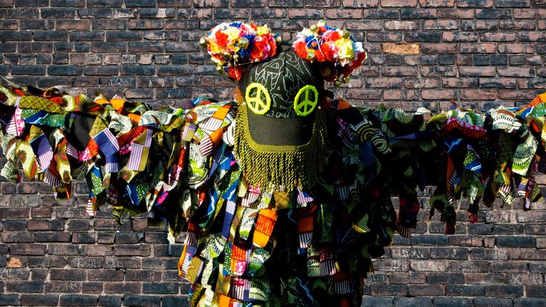 A person wearing a colourful mordern folklore outfit with their arms outstretched against a wall