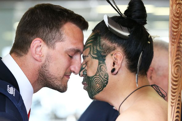 A close-up of Welsh rugby player Sam Warburton receiving a 'hongi' from a Maori chief. The two men are pressing their noses together with their eyes closed.