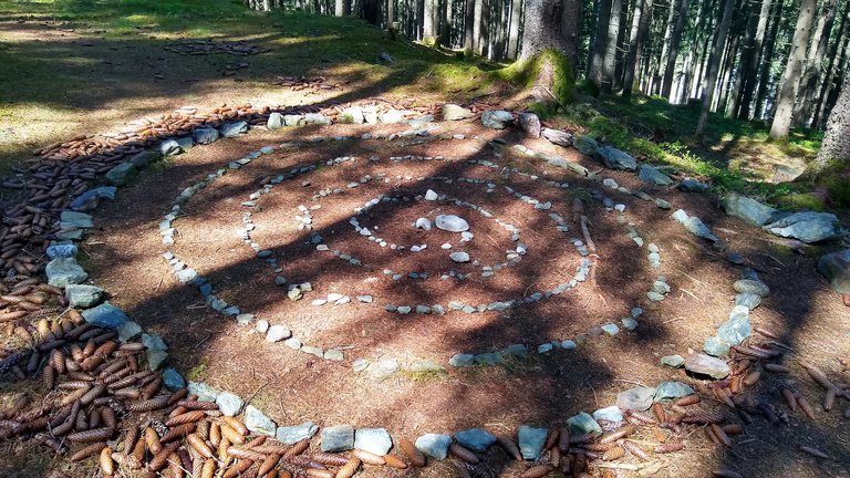 Celtic stone spiral with pine cones in a sunlit forest clearing.