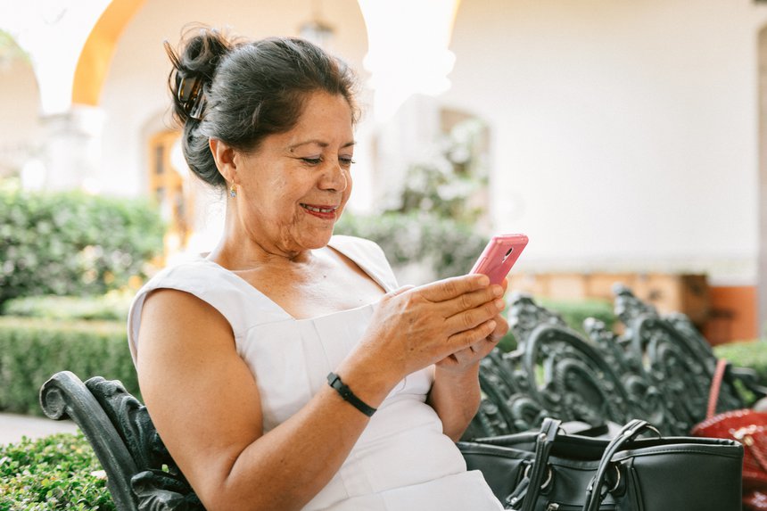 Photograph of a woman sitting down, smiling and looking at the Smartphone in her hand.