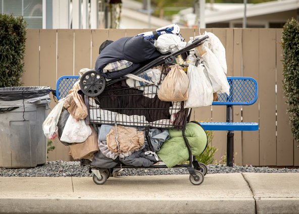 A shopping trolley containing clothing and bedding, next to a bench