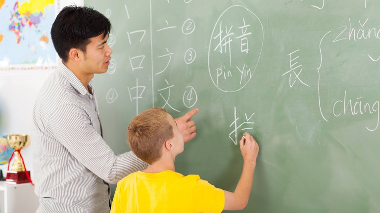 School teacher helping young boy writing chinese