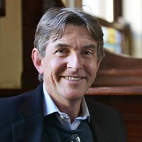 Professor Conor Gearty FBA against a faded interior background, smiling into the camera.