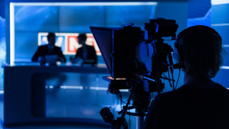 Silhouettes of a camera operator in the foreground and reporters in the background