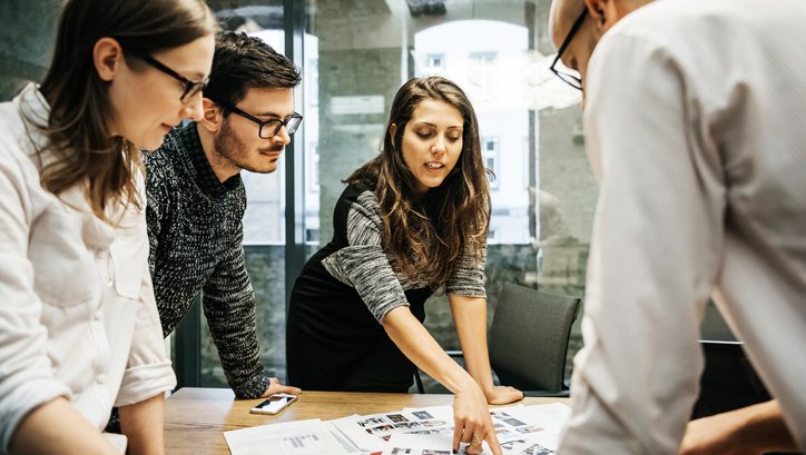 Four people sharing ideas at a table strewn with papers