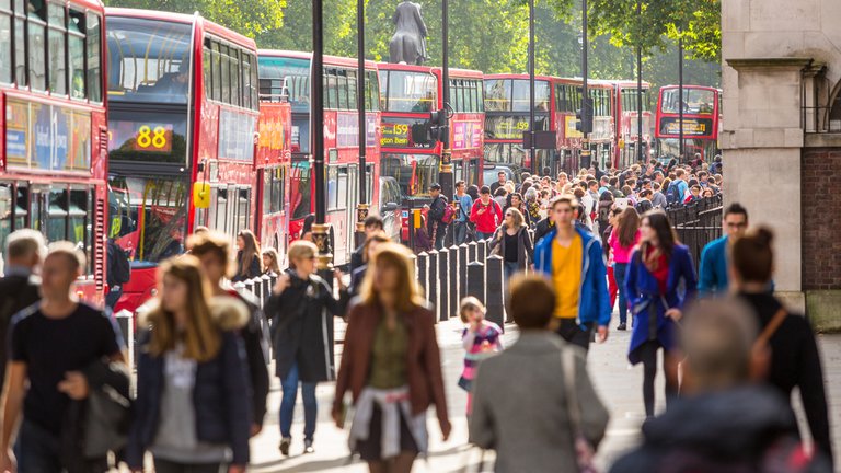 A busy morning outside Brixton Market in South London. The photo shows people walking along the pavement or crossing the road.