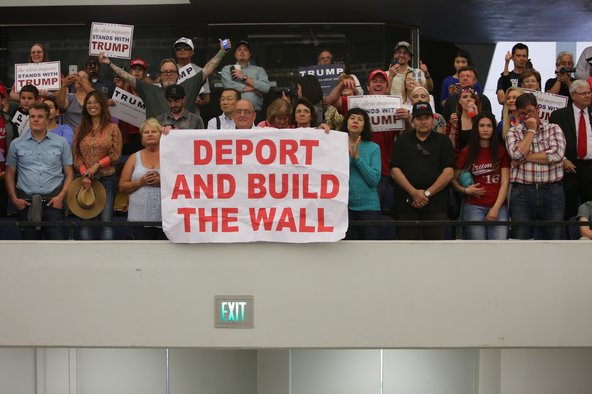 Supporters of US presidential candidate, Donald Trump, hold up a sign bearing the slogan "Deport and build the wall" at a campaign rally at the Anaheim Convention Centre, 2016.