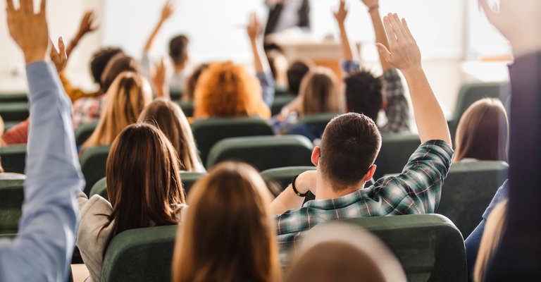 Rear view of large group of students raising arms during a class