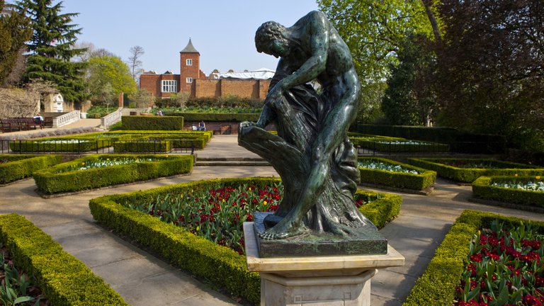 A photograph of Holland Park in London featuring flowers, shrubs and a statue